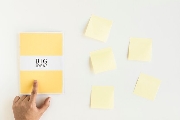 A person's finger over big ideas diary near adhesive notes