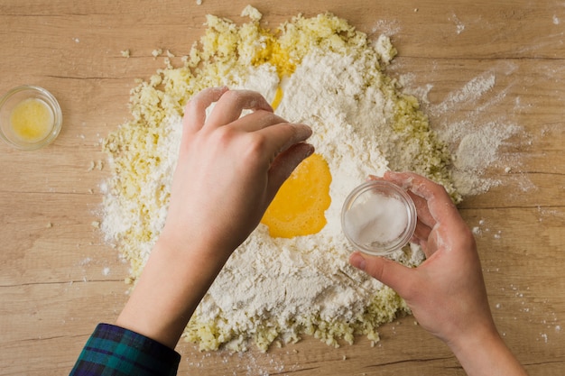 나무 책상에 이탈리아 뇨키를 준비하기 위해 밀가루와 강판 치즈에 소금 꼬집음을 추가하는 사람의 손