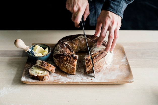 A person's hand cutting baked bagel with sharp knife on chopping board