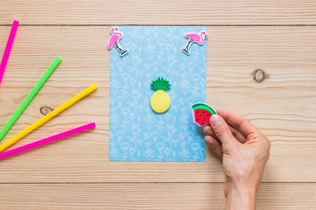 A person's hand decorating blue card with sticker on wooden background