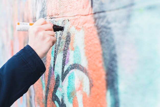 Person's hand drawing graffiti on wall