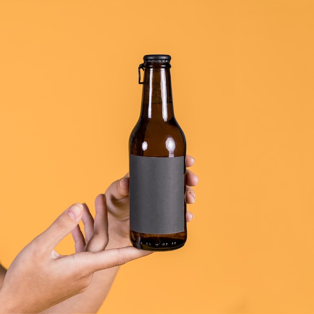 Free photo person's hand holding beer bottle over yellow background