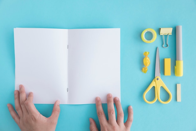 A person's hand holding blank page with stationery and candy on blue backdrop