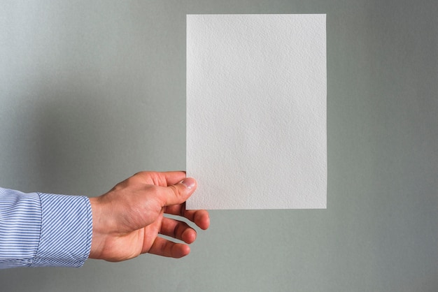 A person's hand holding blank white paper against grey background