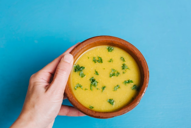 A person's hand holding bowl of pumpkin puree on blue background