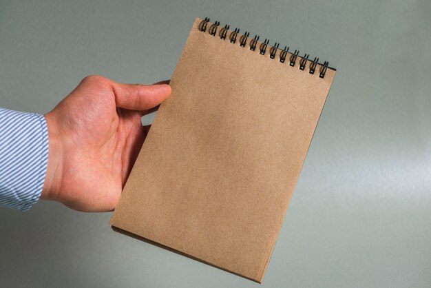 A person's hand holding brown spiral notepad