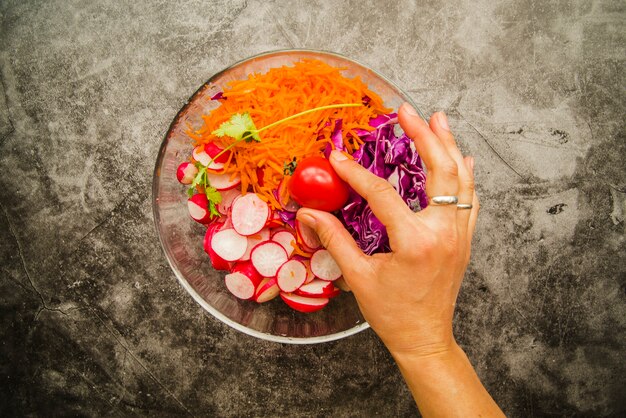 Person's hand holding cherry tomato in fresh salad in bowl