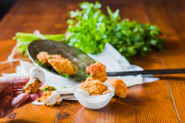 A person's hand holding chicken nuggets dip in garlic sauce