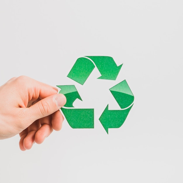 A person's hand holding green recycle symbol on white backdrop