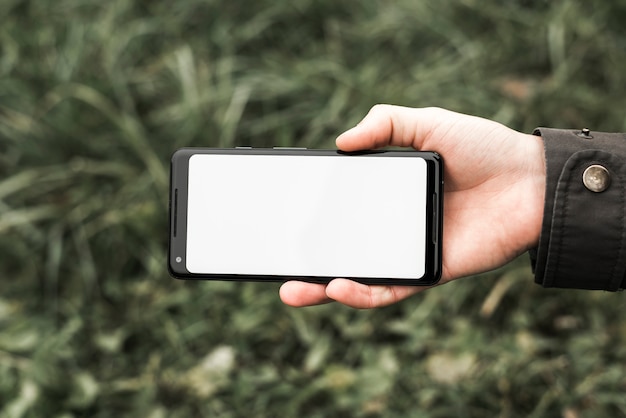 Free photo a person's hand holding mobile phone showing white blank screen display at outdoors