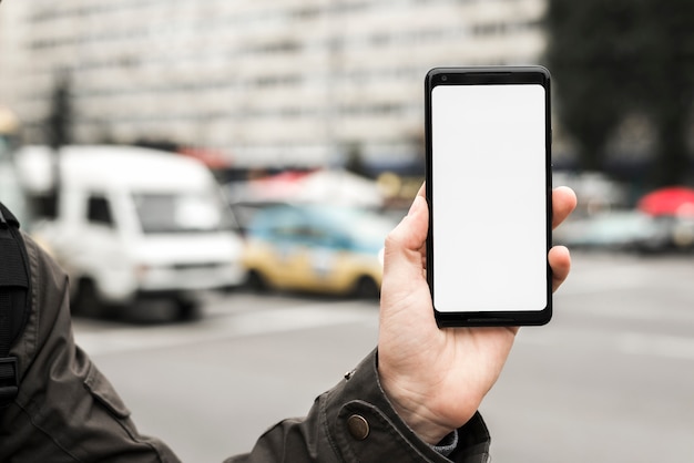 A person's hand holding smart phone showing white blank screen against blurred road