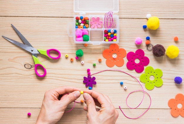 A person's hand making handmade jewelry with beads and flower patch