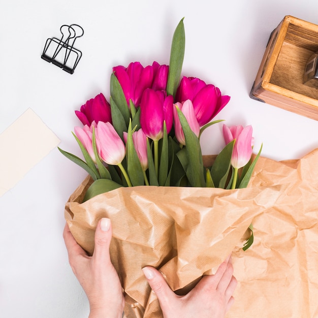 Рука человека делает букет цветов тюльпана с оберточной бумагой на белом фоне