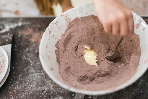 Рука человека, смешивая масло и какао-порошок в миске с помощью ложки