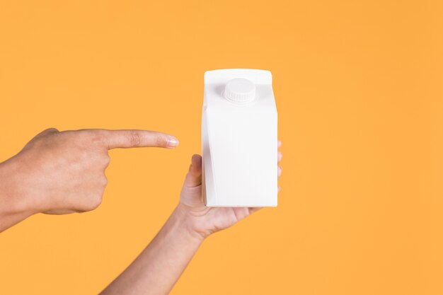 Person's hand pointing over white tetra pack over yellow background