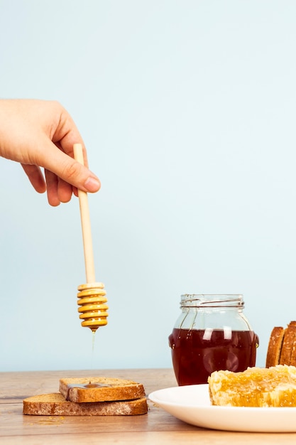 A person's hand pouring honey on bread slice on wooden table
