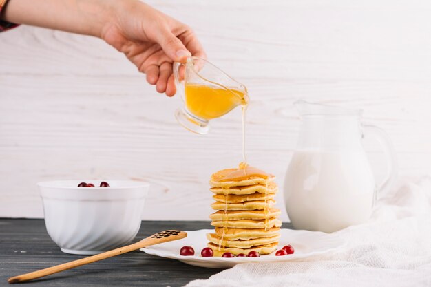 A person's hand pouring honey over the delicious pancakes on wooden table