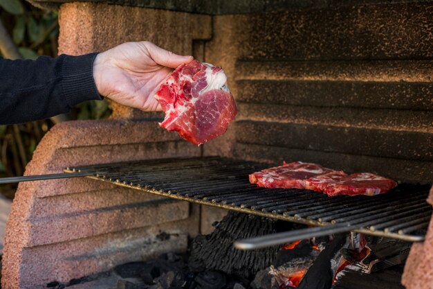 Person's hand preparing raw meat on barbecue grill