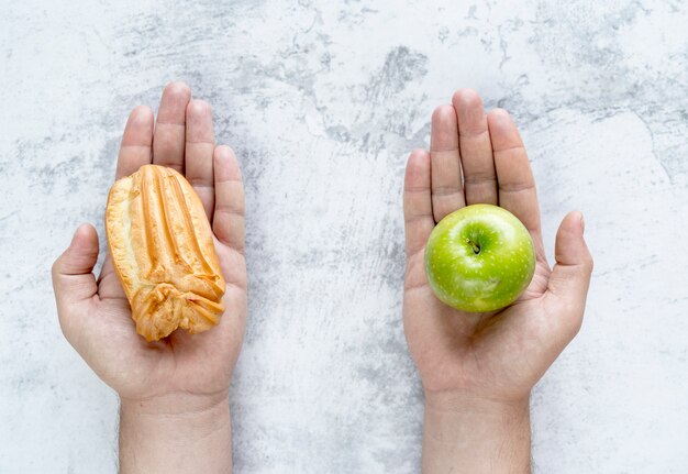 Free photo person's hand showing �clair and green apple over concrete background