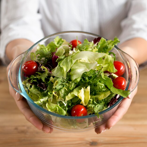 Person's hand showing green leafy vegetable salad with red cherry tomatoes