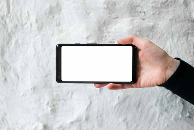 A person's hand showing mobile phone screen display against white concrete wall