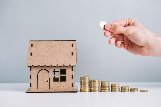 A person's hand stacking coins near house model