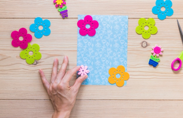 A person's hand sticking flower patch on scrapbook card