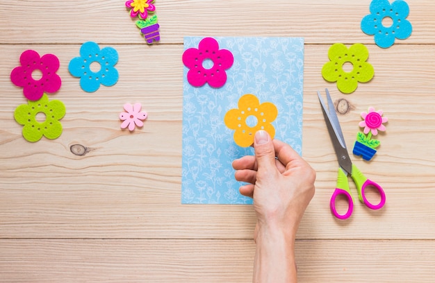 A person's hand sticking flower sticker on scrapbook paper