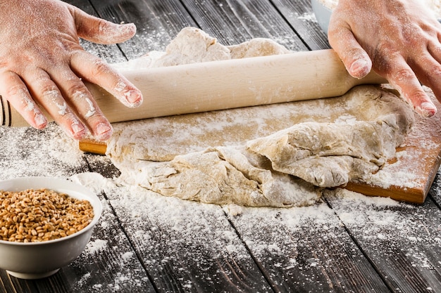 A person's hand stretching the dough with rolling pin on the kitchen table