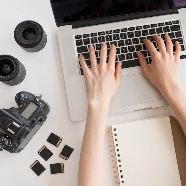 Person's hand typing on laptop keyboard with camera accessories and spiral book