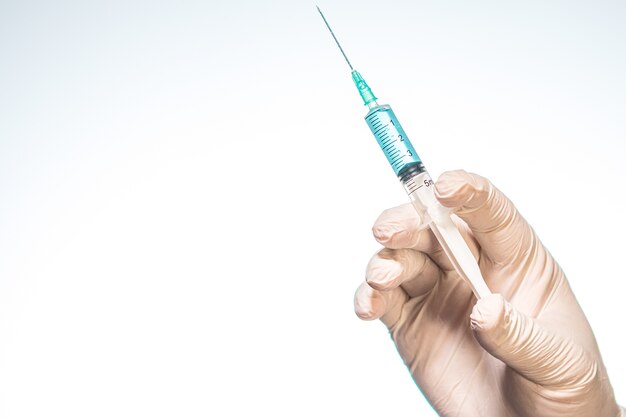 Person's hand wearing a surgical glove and holding a syringe with a white background