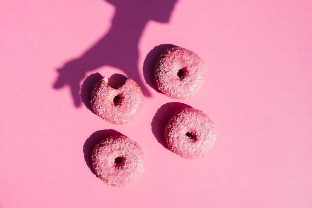 A person's shadow near the donuts on pink background