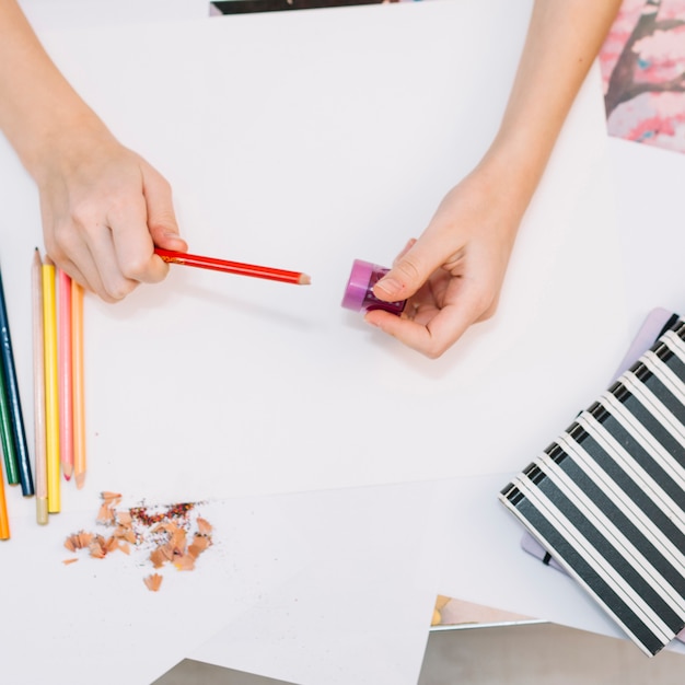 Person sharpening red pencil at table 