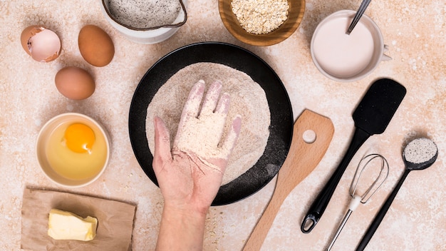 Foto gratuita una persona che mostra la farina nel piatto con gli ingredienti del pane sullo sfondo