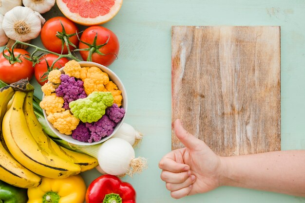 A person showing thumbsup sign over the chopping table and fresh healthy food