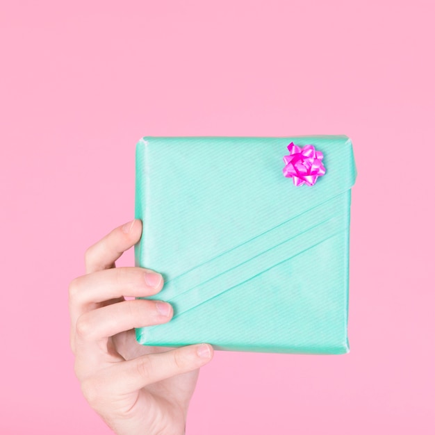 A person showing wrapped turquoise gift box on pink background