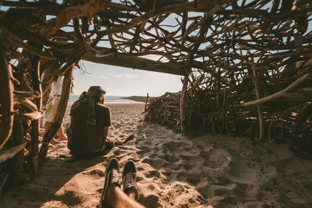 海の近くの砂の上に座っている人の写真を撮る木製の洞窟の中に座っている人