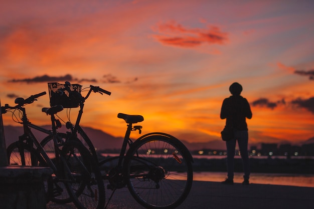 Person standing at bicycle in sunset