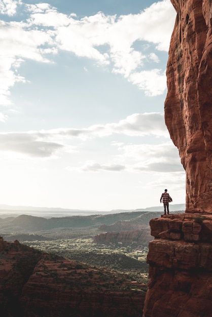 A person standing at the edge of a cliff surrounded by hills and mountains under a clear sky