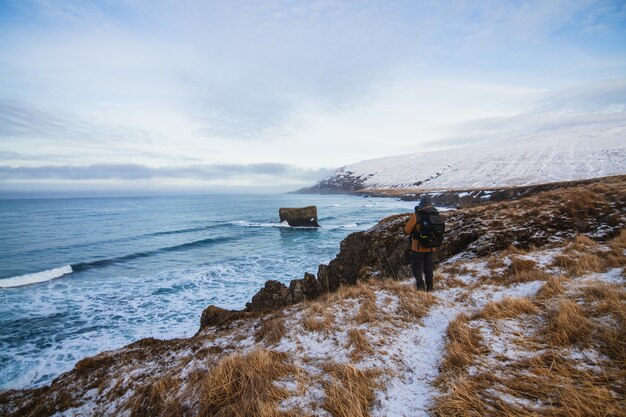 Человек, стоящий на холмах, покрытых снегом, в окружении моря в Исландии
