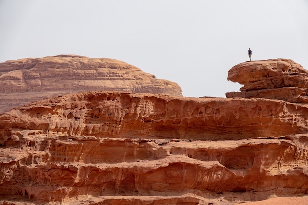 Free photo person standing on a large cliff in a desert under a cloudy sky
