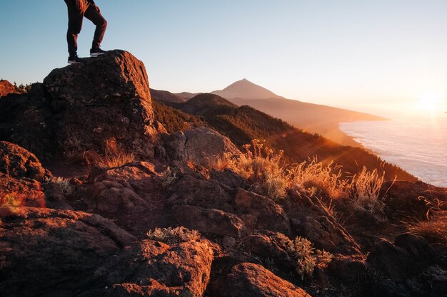 明るい夕日の間に海に囲まれた岩の上に立っている人-成功の概念