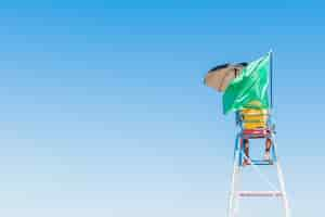 Free photo person standing on the security seat at the beach with a waving green flag