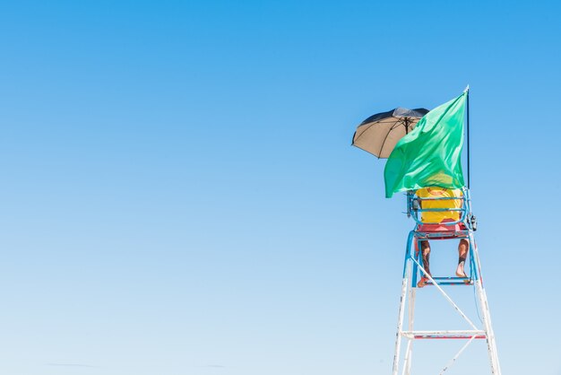 Person standing on the security seat at the beach with a waving green flag