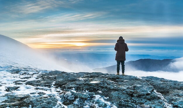 夕日の下の山々の息を呑むような景色の上の雪に覆われた崖の上に立っている人