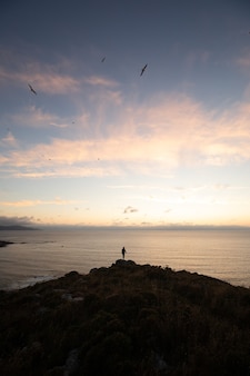 Person standing on top of a hill by the sea at sunset - success concept