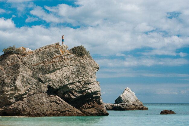 Человек, стоящий на вершине скалы в окружении водоема в дневное время