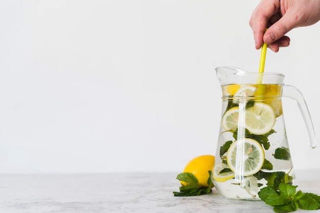 Person stirring lemon drink with mint in jug