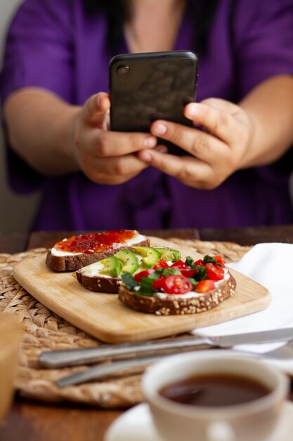 Человек, фотографирующий ассортимент бутербродов со смартфоном