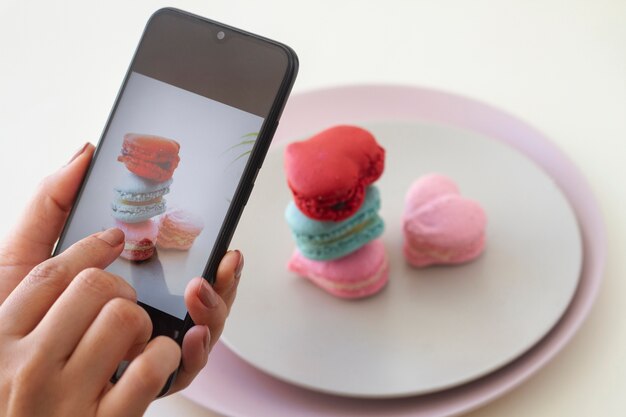 Person taking photo of heart-shaped macarons on plates with smartphone